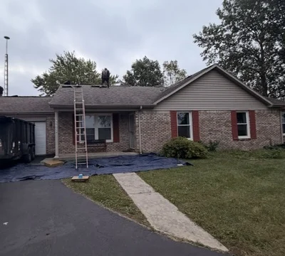The same brick ranch on tear-off day, with ladder, tarps and crew on the roof