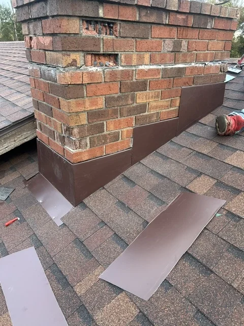 New metal flashing going in around a brick chimney on a shingle roof
