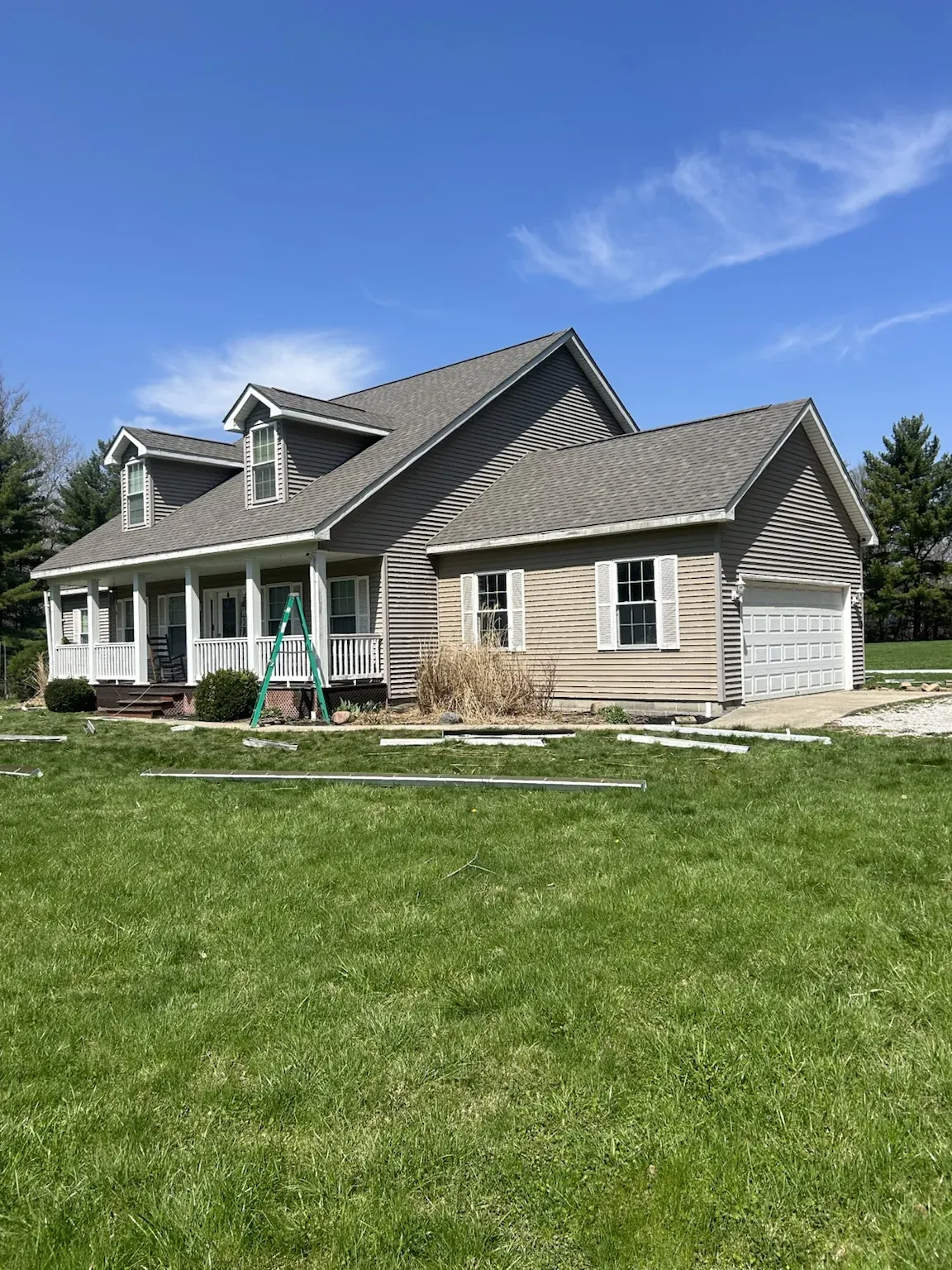 Finished two-story Cape Cod style home with two dormers, a full-width front porch and an attached garage, with a new gray architectural shingle roof
