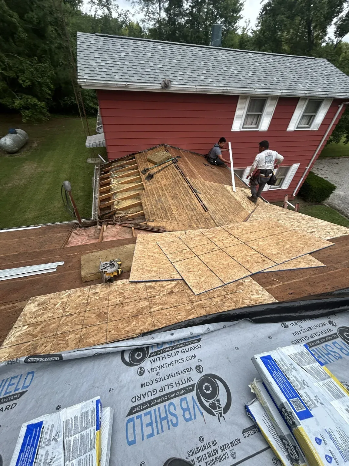 Red two-story home during tear-off, with the old board decking exposed, new OSB sheathing going down over it and rolls of synthetic underlayment ready
