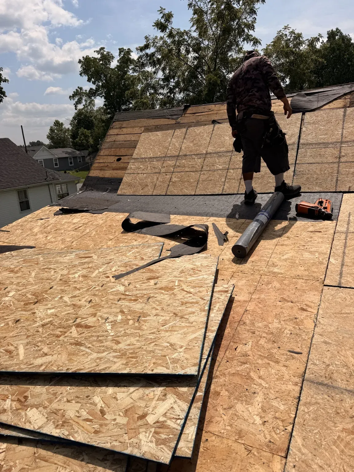 Roofer standing on new OSB decking, with more sheets stacked and a roll of underlayment ready after the old roof was stripped