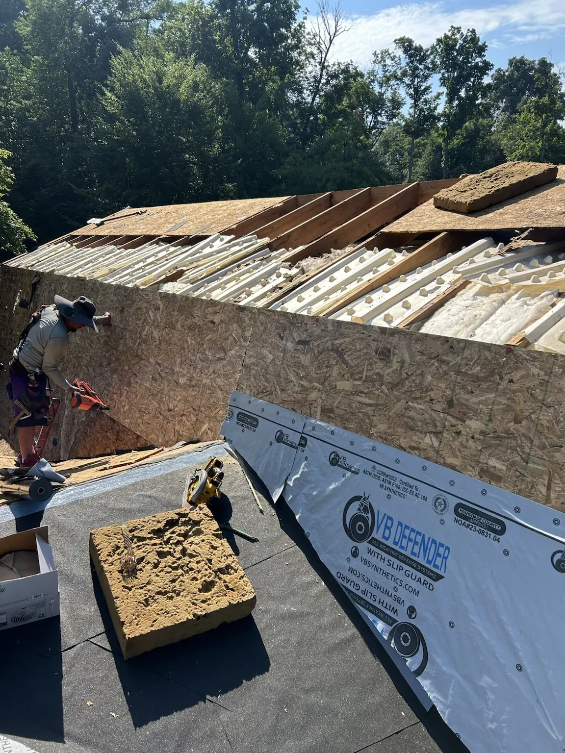 Crew working where a lower roof meets the upper level during a tear-off, with new underlayment going down on the lower roof