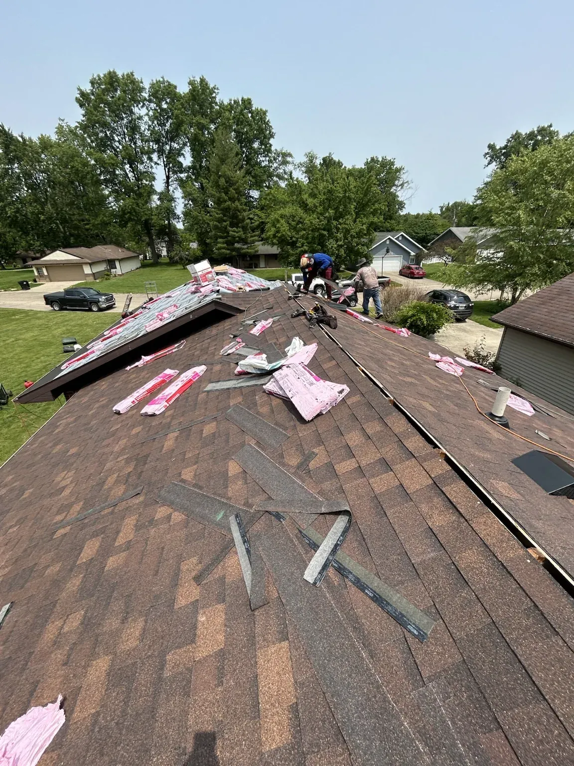 Crew stripping an older brown shingle roof, with torn-off shingles and debris across the slope