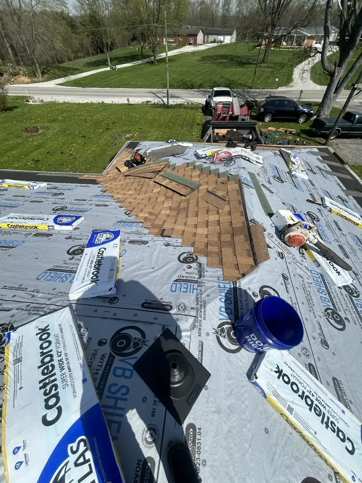 Synthetic underlayment rolled out with Atlas shingle bundles staged on top, a pipe boot in place and part of the old roof still being stripped