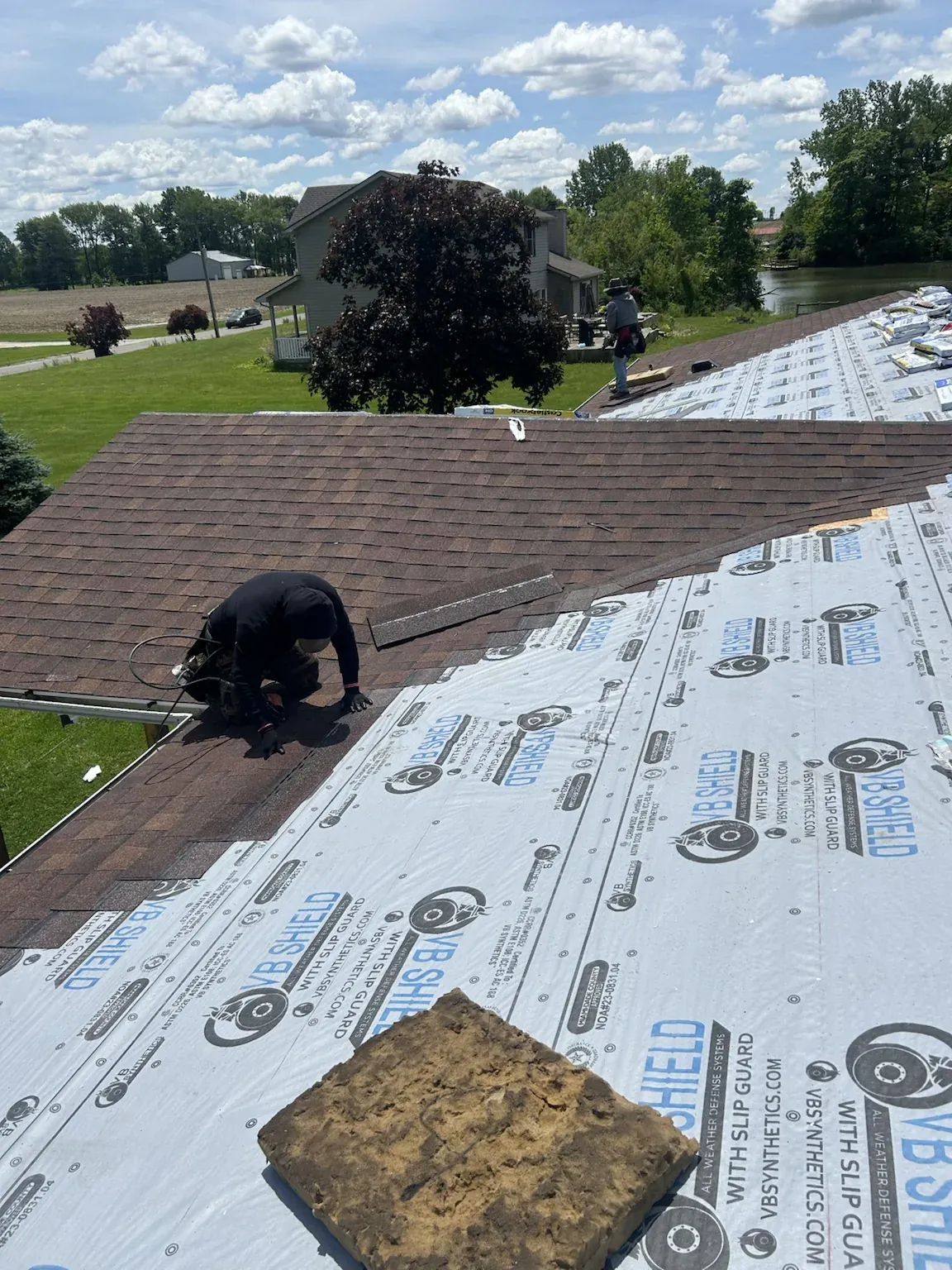 Roofer rolling out synthetic underlayment over the decking beside a section of old brown shingles