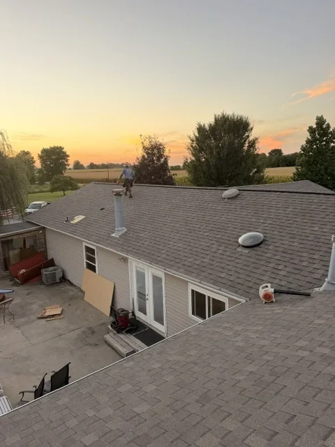 Shingle roof with vents at sunset, crew member on the ridge